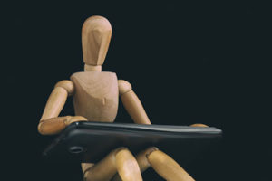Artist wood figure model, seated working at (enlarged) keyboard