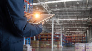 Worker torso on tablet with highlighted logo, superimposed world map over warehouse background