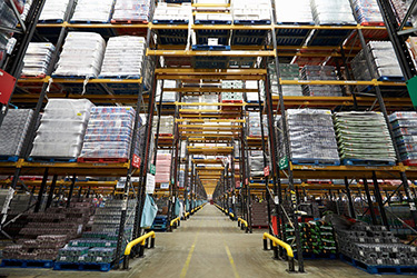 Looking down aisle between tall storage racks of full warehouse